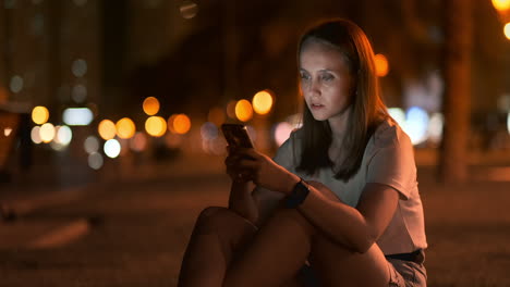 Una-Hermosa-Joven-En-Verano-En-Una-Gran-Ciudad-Nocturna-Mantiene-Un-Teléfono-Inteligente-En-Su-Interior-Y-Escribe-Un-Mensaje-Lee-Correos-Electrónicos-Y-Se-Comunica-En-Salas-De-Chat-Y-Redes-Sociales-Mantiene-Un-Blog-Mira-La-Pantalla-Del-Teléfono